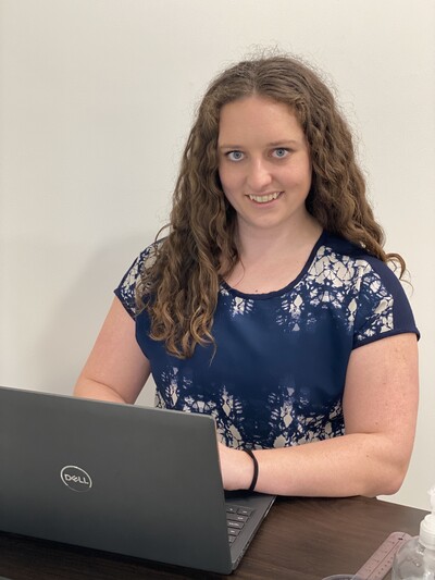 Team member of Nova Physiotherapy in Warman sitting at a desk in the clinic working on a laptop. She is smiling and demonstrating how to book online consultations.