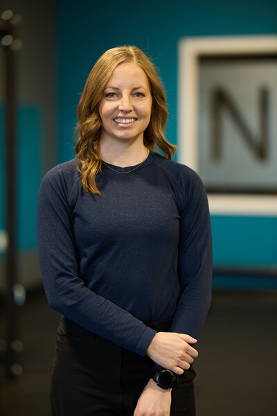 Nova team member and physiotherapist standing in clinic gym in front of Nova window wearing blue long sleeve