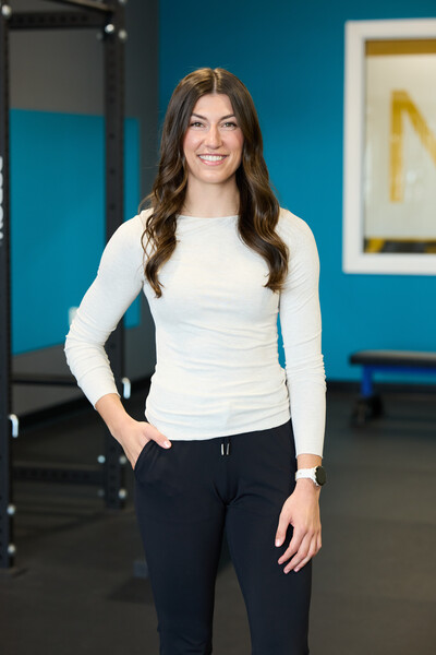 Team member and physiotherapist standing in clinic gym in white shirt with blue wall behind