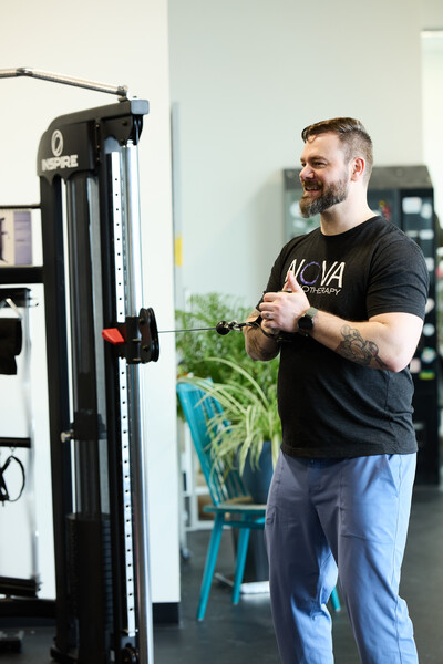 one man wearing black shirt and standing in clinic gym holding handle for cable machine