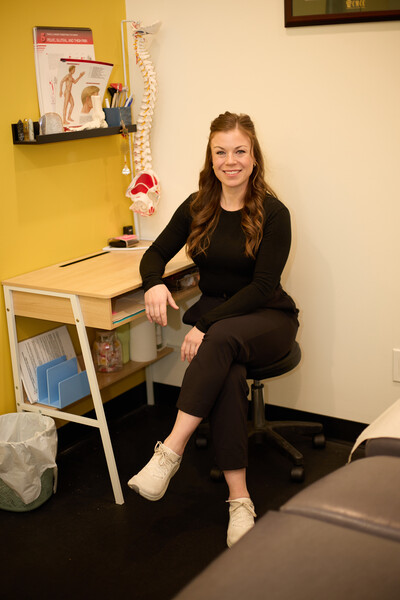Nova team member and chiropractor sitting in clinic treatment room at desk with treatment bed