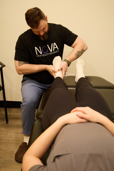 One man who is a physiotherapist and wearing a black shirt holding client foot to provide hands on treatment