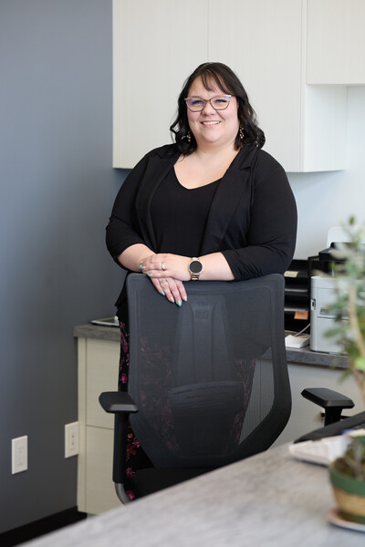 Woman standing in front reception area behind black chair with grey wall and reception drawers behind