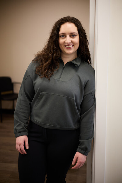 Team member and physiotherapist leaning against treatment room door wearing green sweater