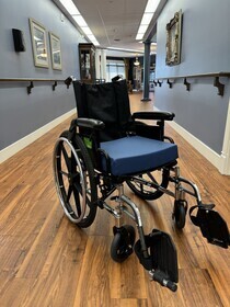 Blue and black wheel chair sitting in hallway of Nova Physiotherapy clinic in Warman. Hallway has blue walls with wood flooring. 