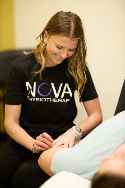 team member and physiotherapist wearing grey nova shirt providing dry needling to women elbow who is wearing blue shirt
