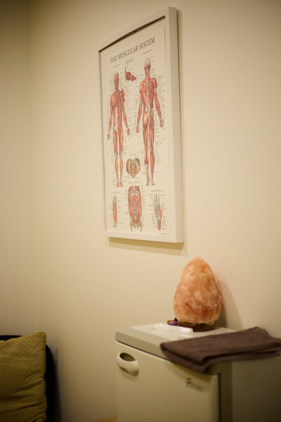black chair, white poster of anatomy muscles, pink crystal on top of white box for massage therapy tools